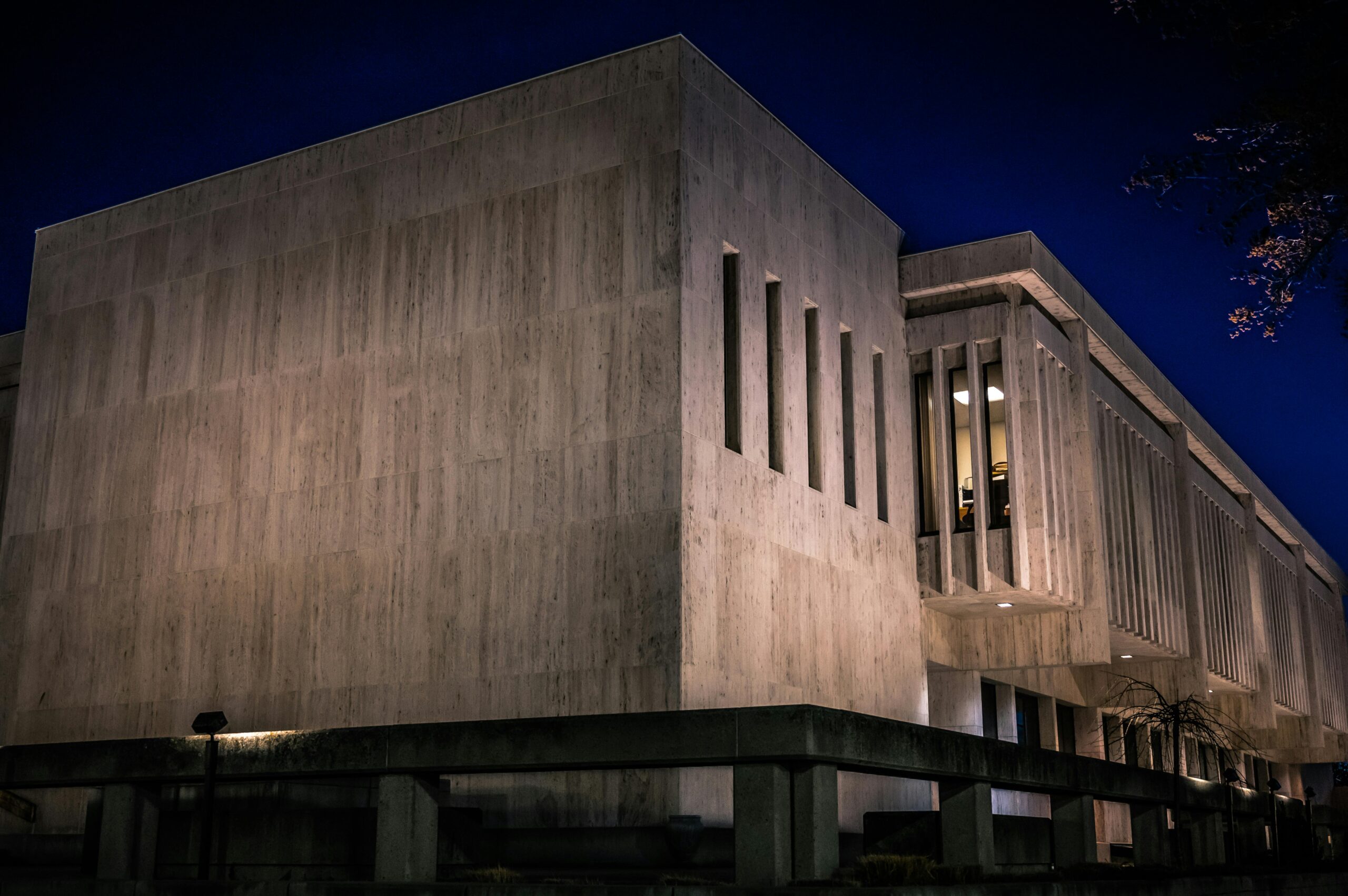 A modern concrete building illuminated against a deep blue night sky, showcasing strong lines and shadows.