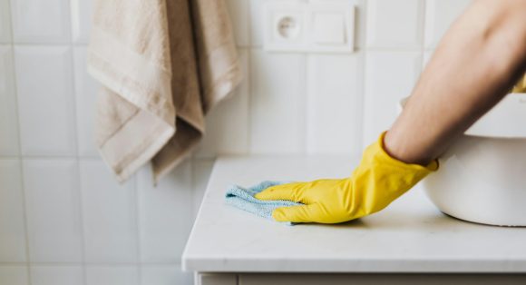 pexels-photo-4239037-4239037 Close-up of a person wearing yellow gloves wiping a bathroom counter with a cloth.